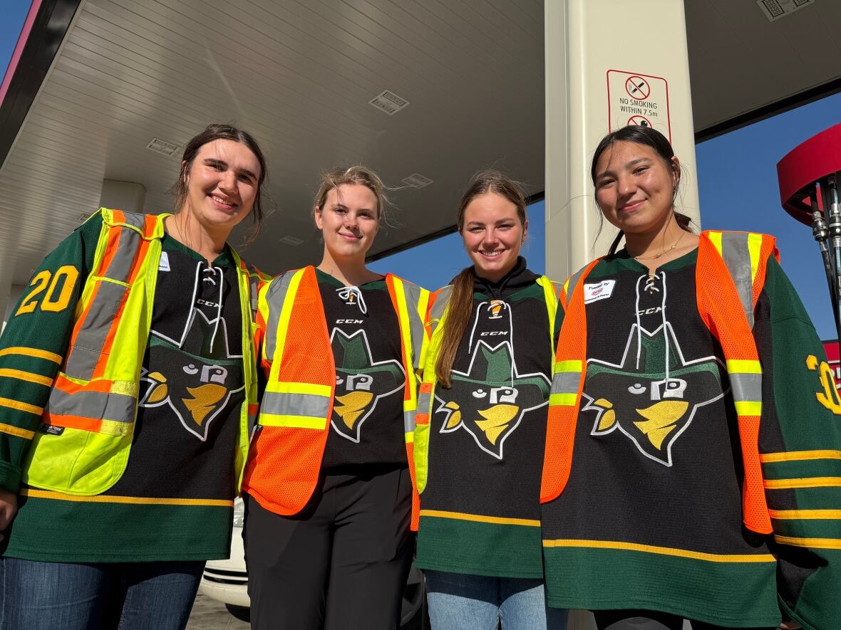 Four people standing at a gas station.