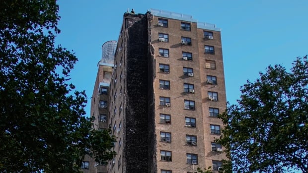 A tall apartment building is seen from the ground, with part of its facade ripped out.