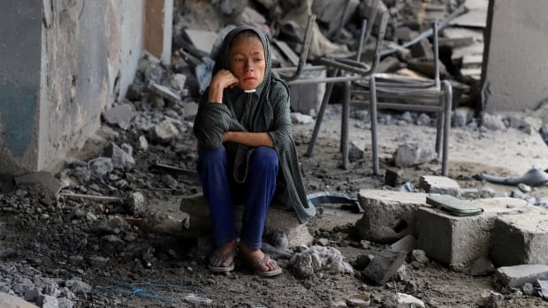 A girl sits amid debris.