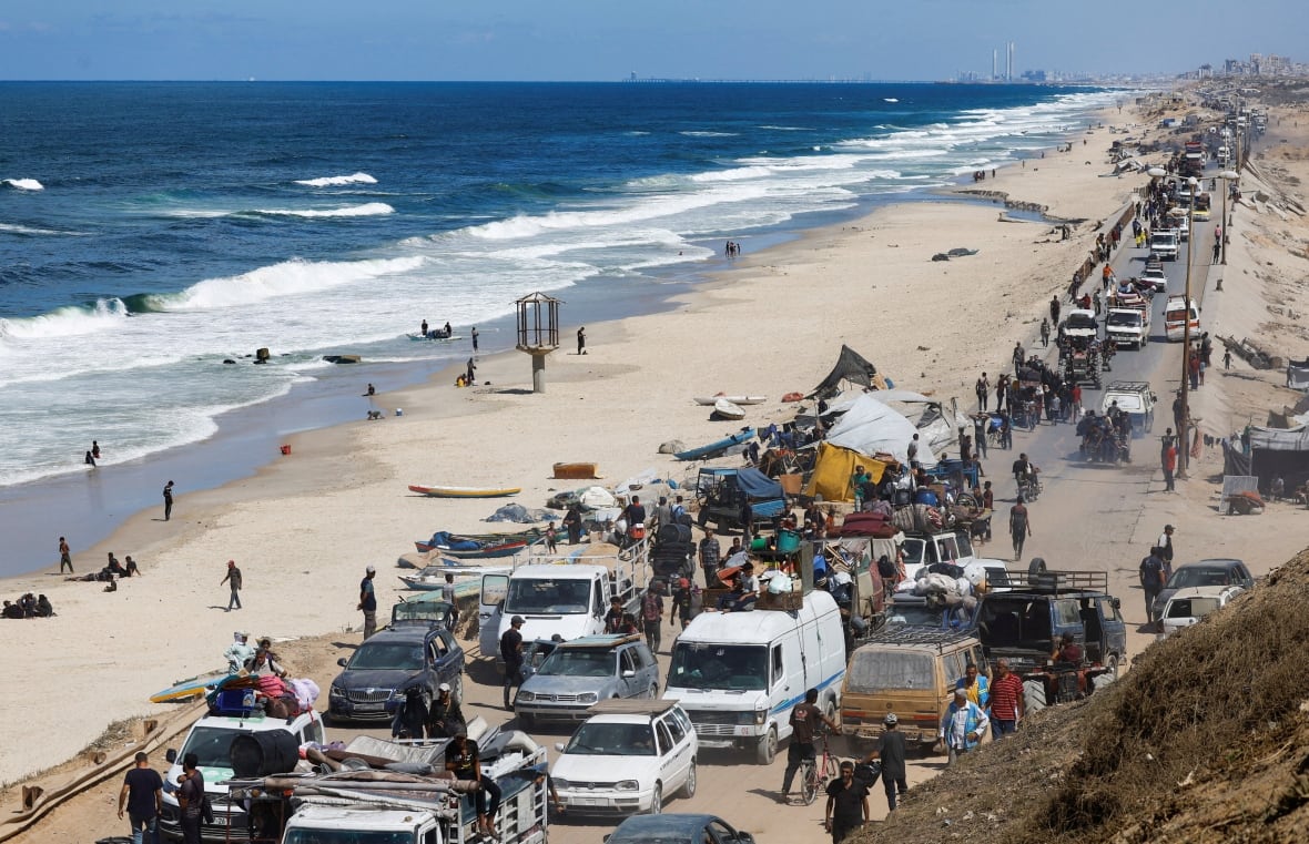 A long line of vehicles standing on a crowded road on the beach.