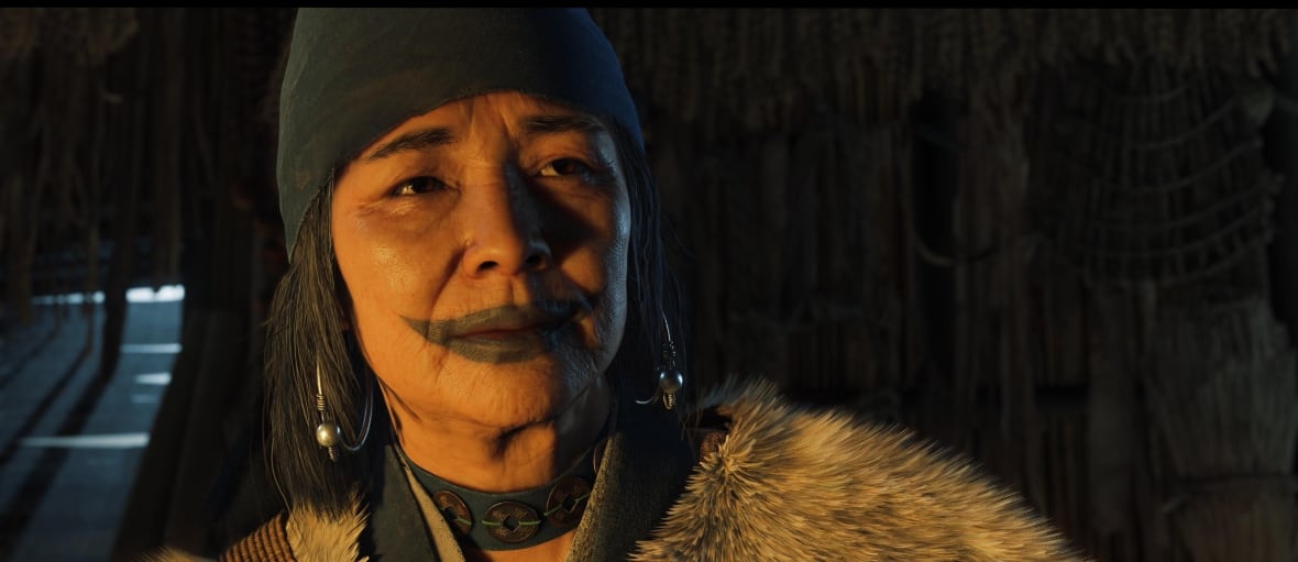 Screenshot di un videogioco che ritrae un'anziana donna giapponese Ainu con un tatuaggio tradizionale sul viso.