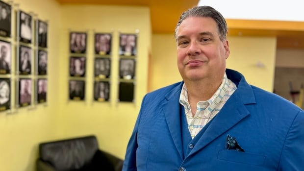 A man with salt and pepper hair and a blue suit looks at the camera. 