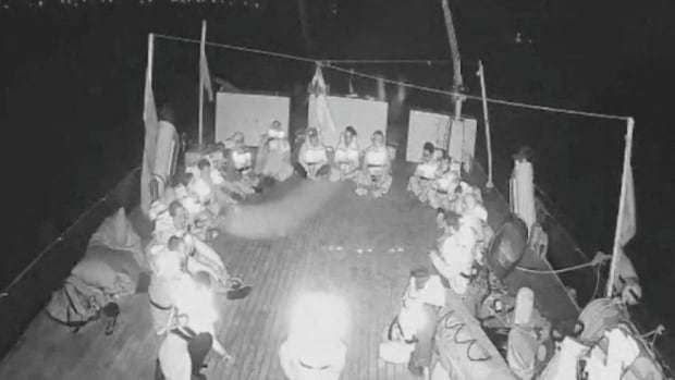 Grainy black and white image of a boat deck with people seated in a circle