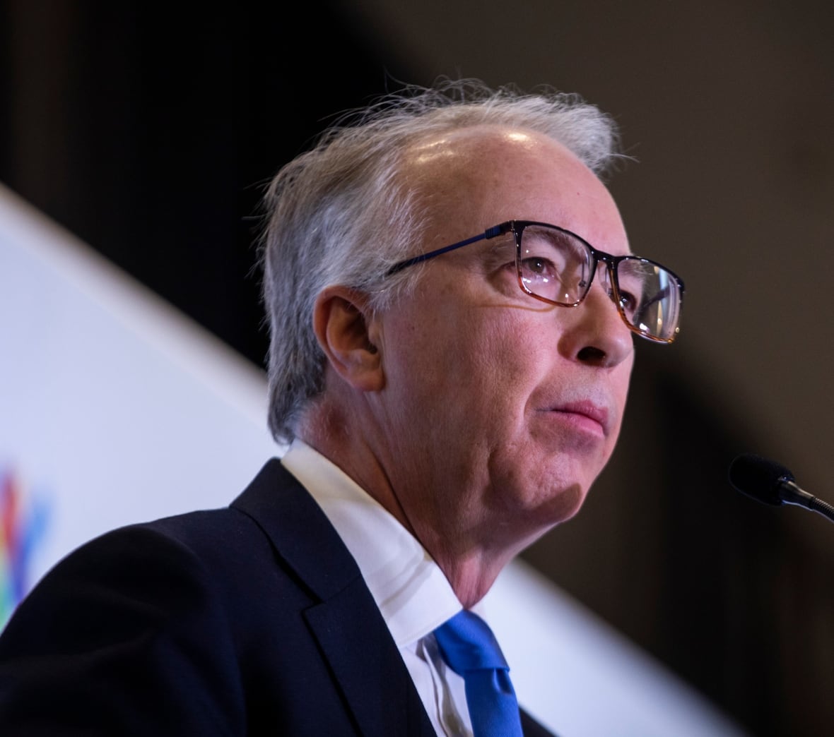 A man wearing glasses speaks at a microphone.