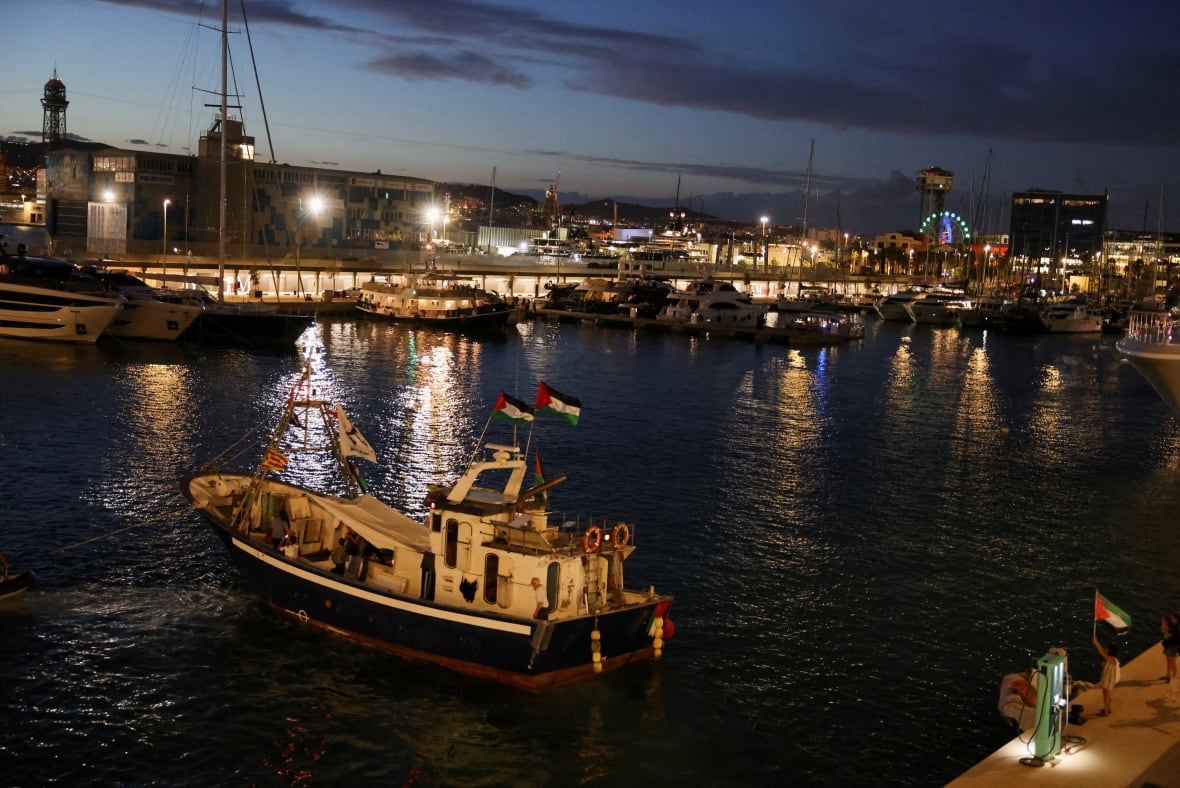 A night image of a boat sailing from a port with red, white and green flags that fly