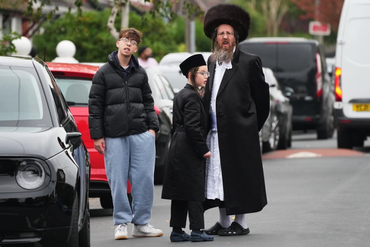 A man and two young boys appear standing on a street near the vehicles. 