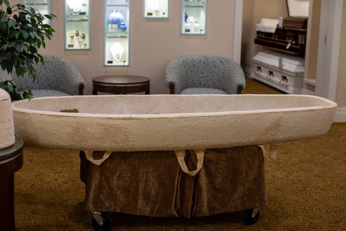 Coffin made of fungus with traditional coffins in room behind it