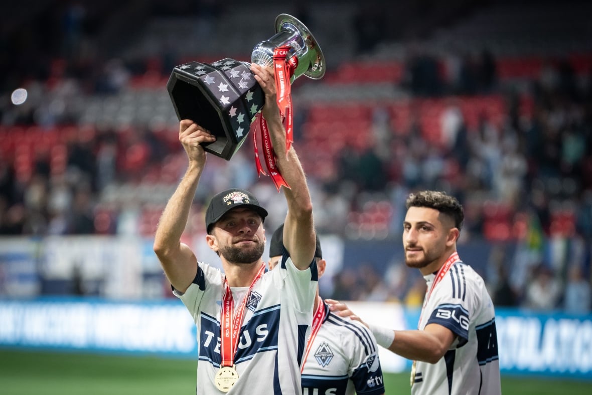 Thomas Müller, wearing a black baseball hat and a medal hoists a silver cup.