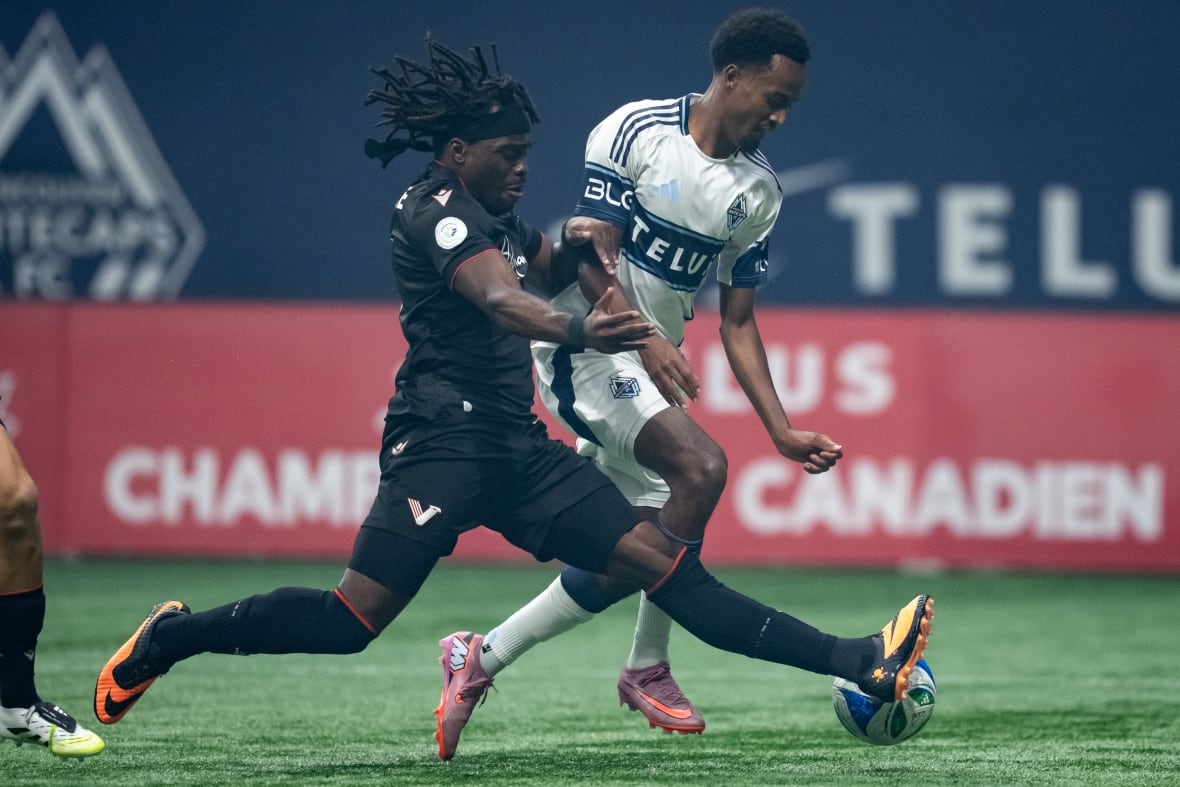 Two soccer players, one in a black uniform, the other in a white and blue uniform come together over a white blue and green soccer ball.