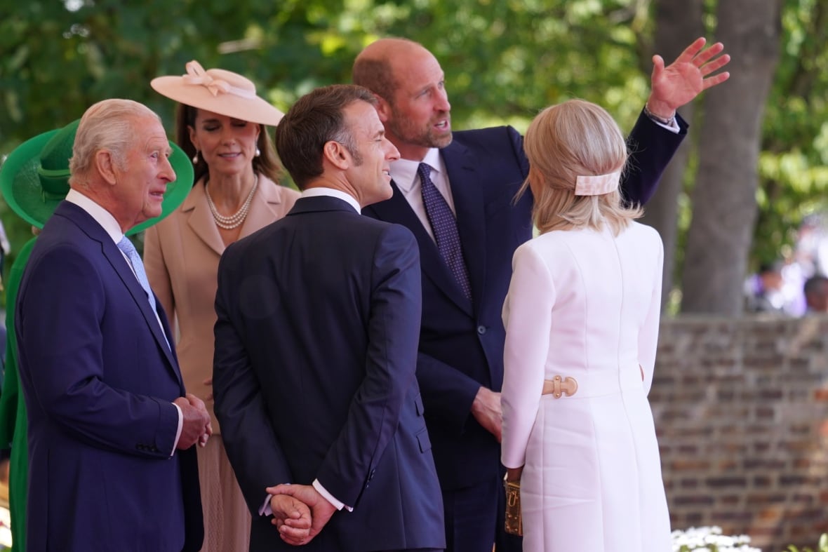 Several people stand talking while one holds one arm up gesturing toward the distance.