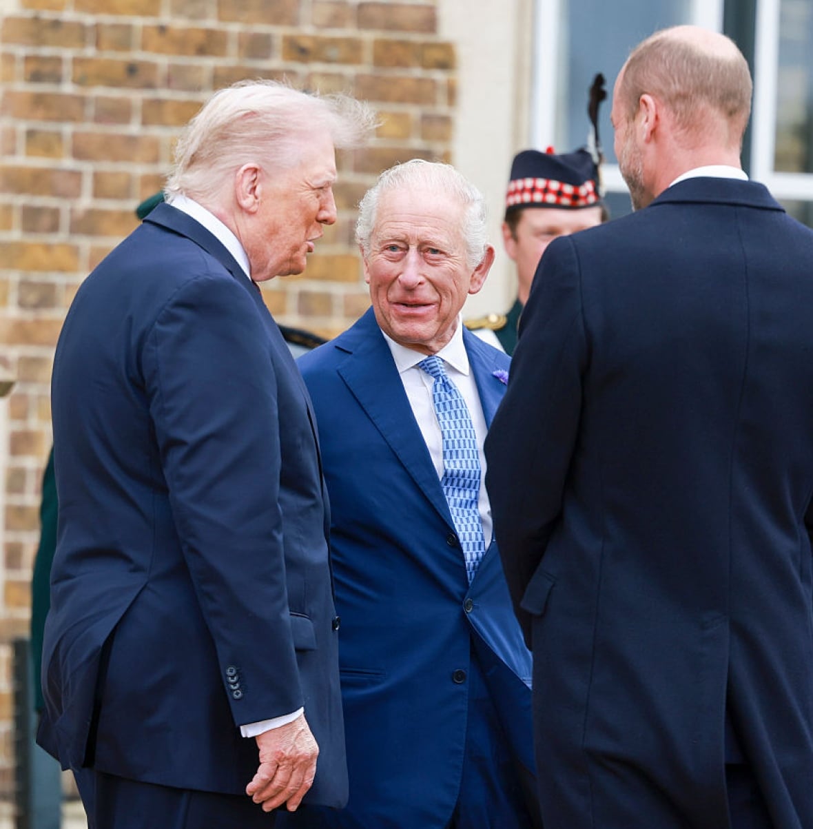 Three people talk with one another as they stand outside a brick building.