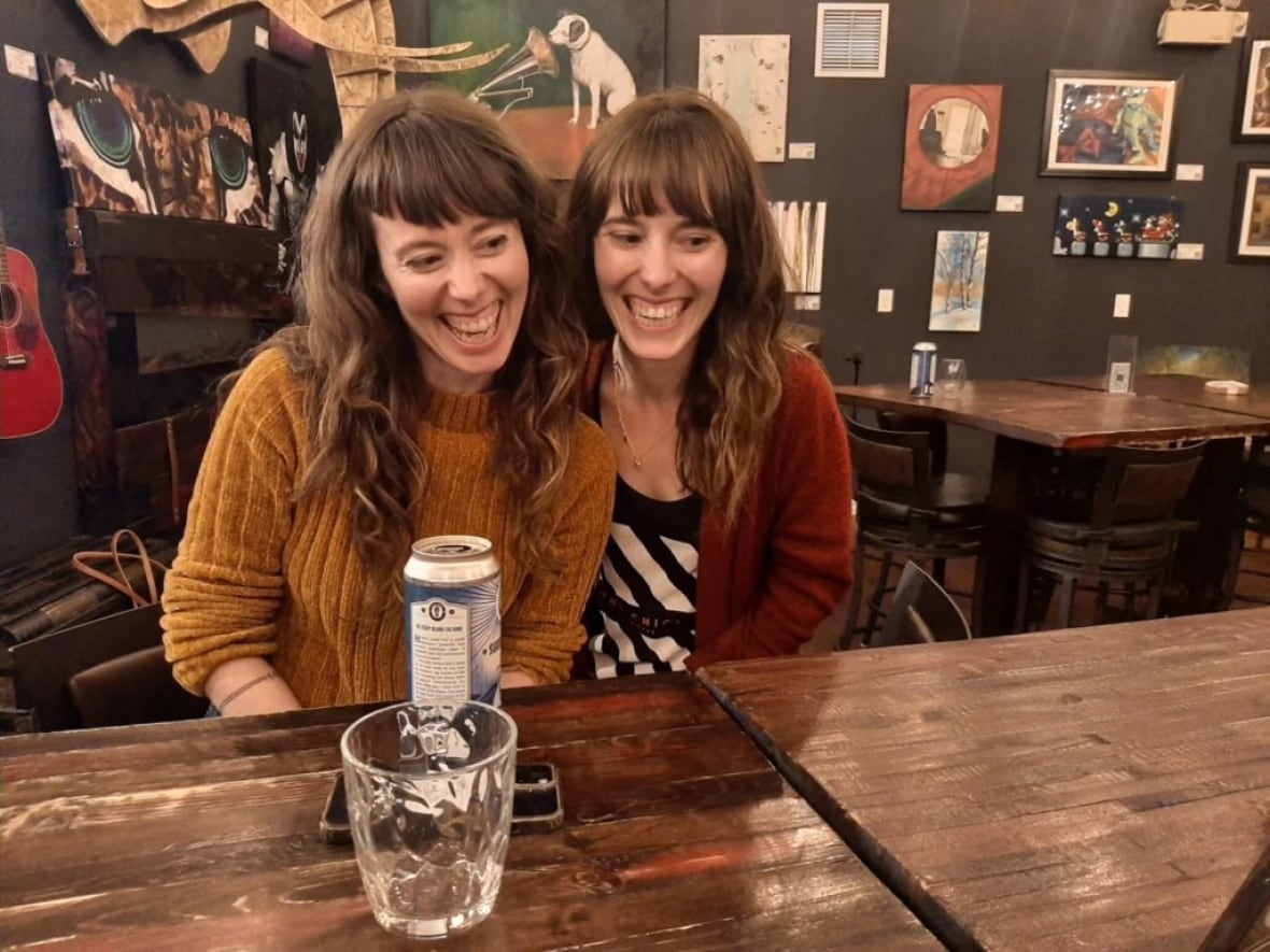Two women pose behind a table, smiling and posing the same way.