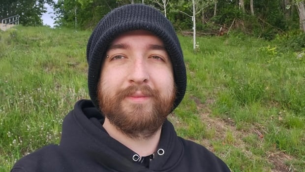 A young man with a beard wearing a black toque and a black hoodie. 