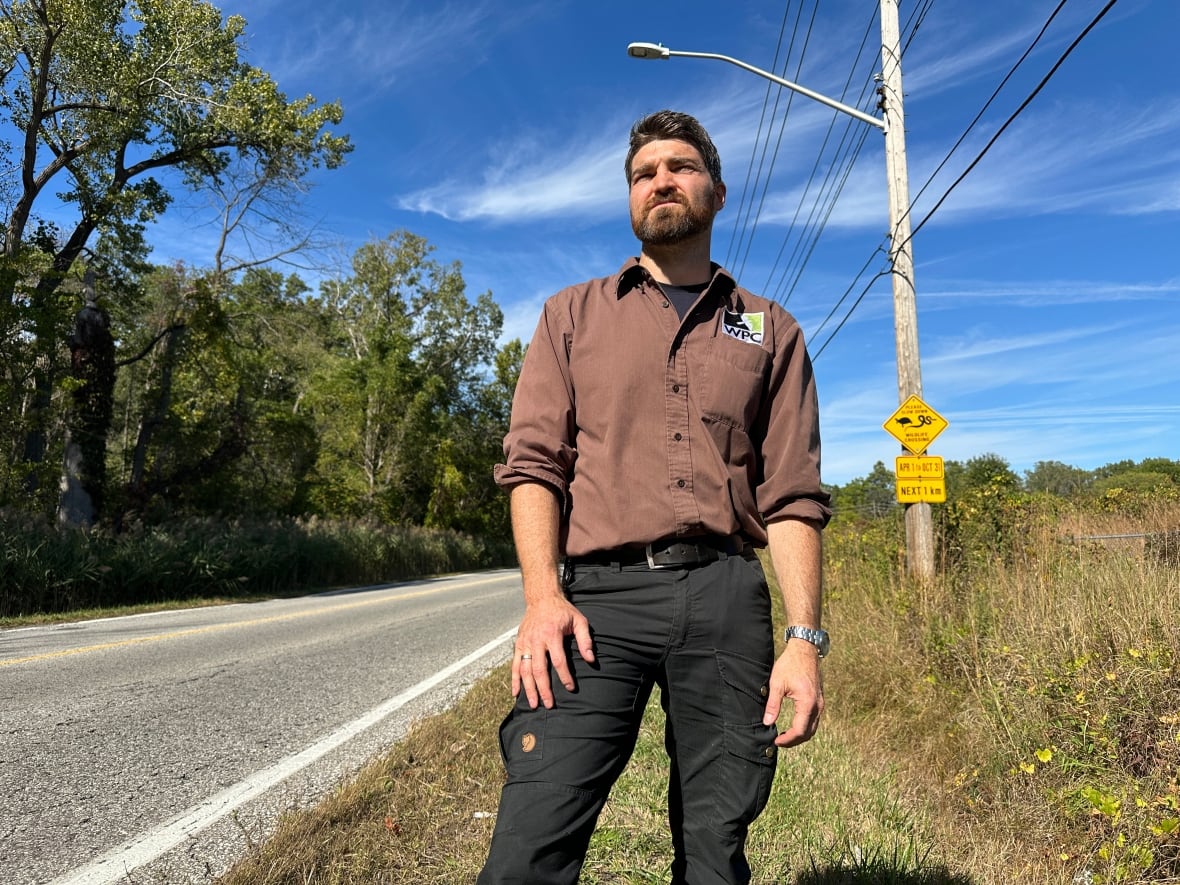 A man stands next to a roadway.