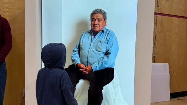 A child stands with his back to the camera facing a machine about the size of a large vending machine with a glass front and a person (actually a hologram of a person) seated inside. 