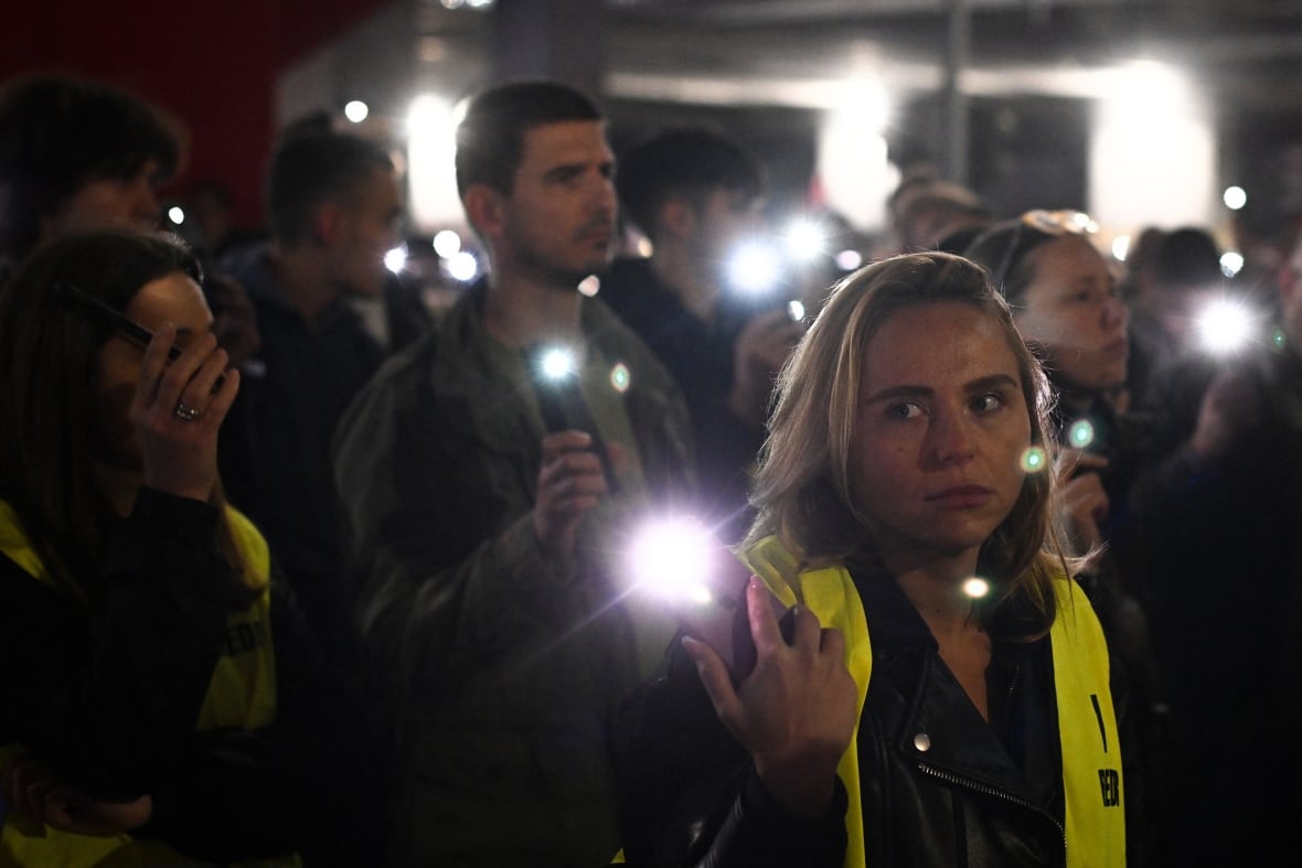 People standing in the dark and hold cell phones with flashlights