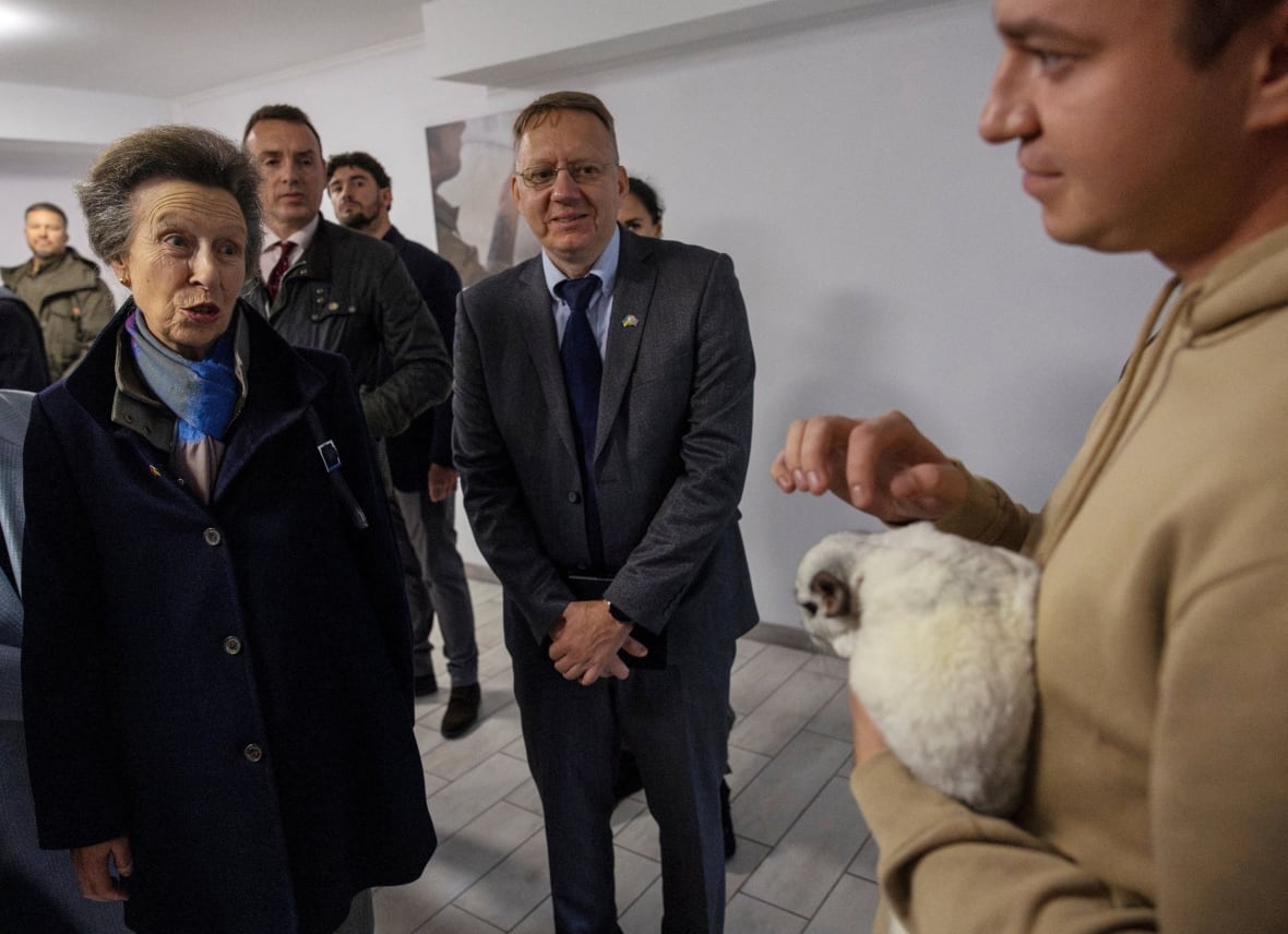 A person talks to another person holding an animal as other people look on.