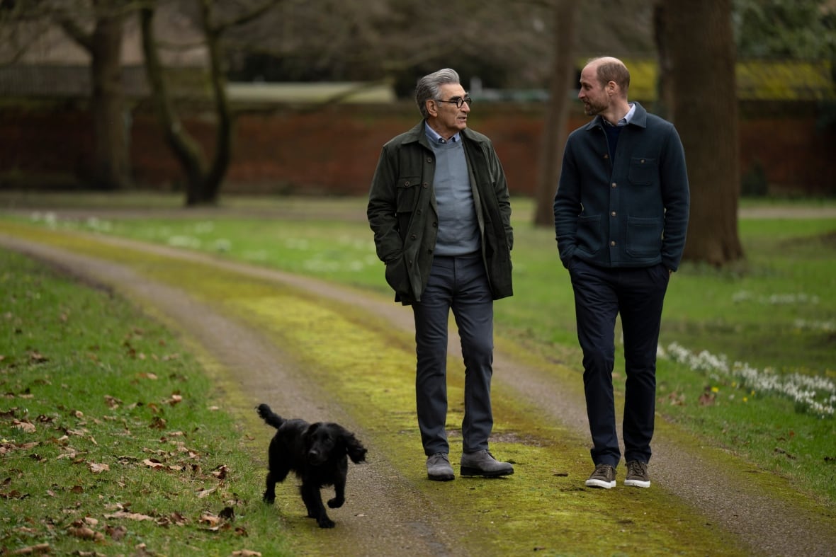 Two people talk while they walk along a vehicle track with a black dog.
