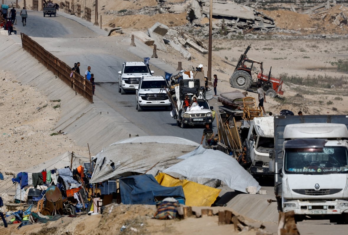 United Nations vehicles lead to a road as displaced Palestinians, fleeing northern Gaza due to an Israeli military operation, walk nearby.