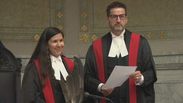 A woman and man in judge's attire stand.