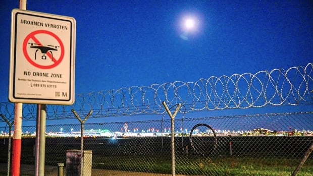 A sign signally the prohibition of drone use is seen near a fence outside an airport.