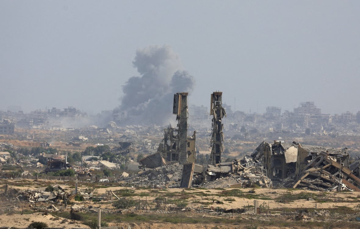 Smoke rises amid rubble from afar.