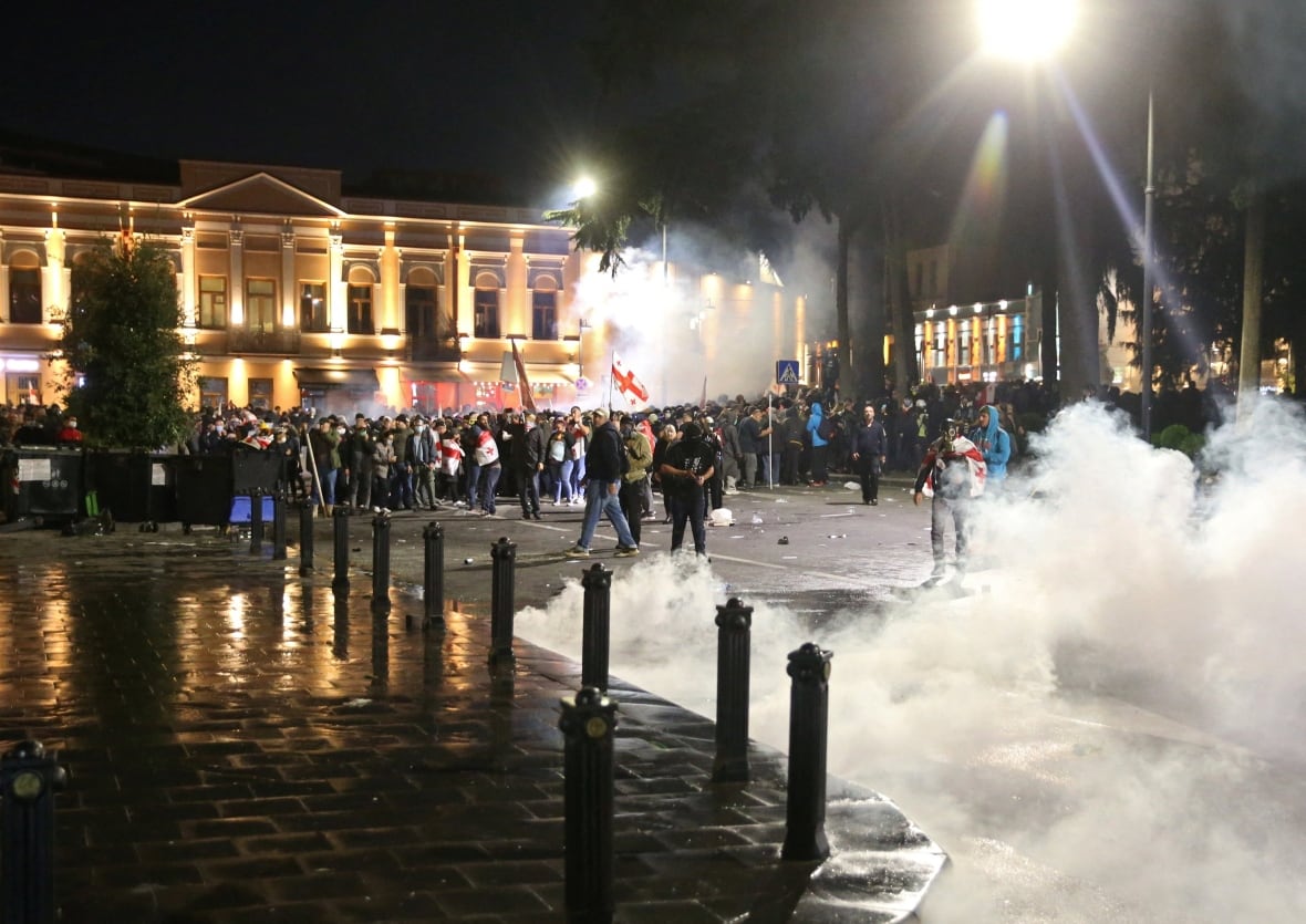 The demonstrators come together while tear gas smoke rises in the street.