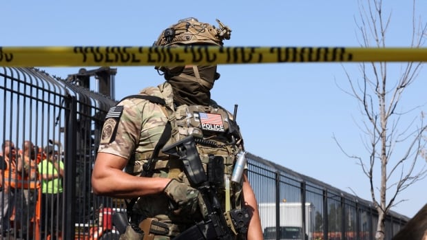 An armed officer stands guard behind police tape.