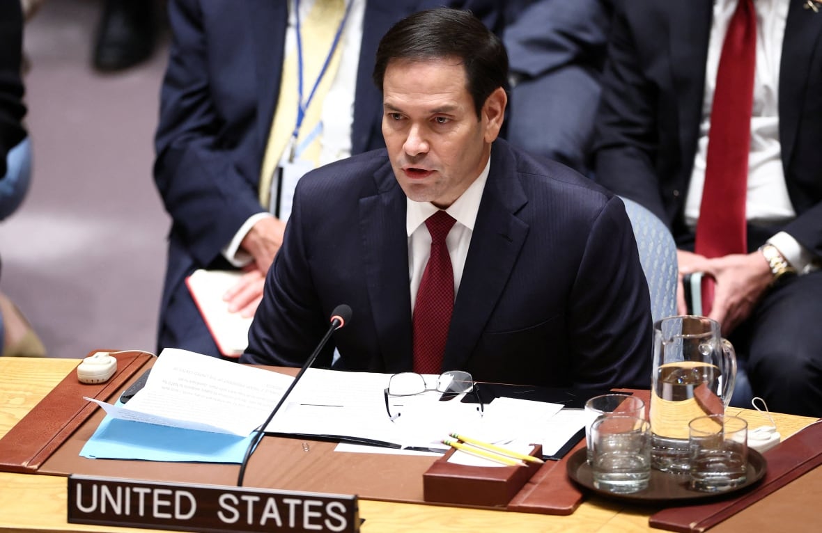 A black hair man wearing a navy suit is on a desk and talks to a microphone.