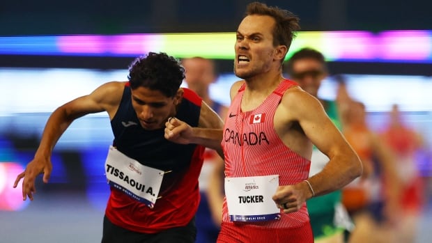 A male competitive runner representing Canada pumps his right fist in celebration as he crosses the finish line.