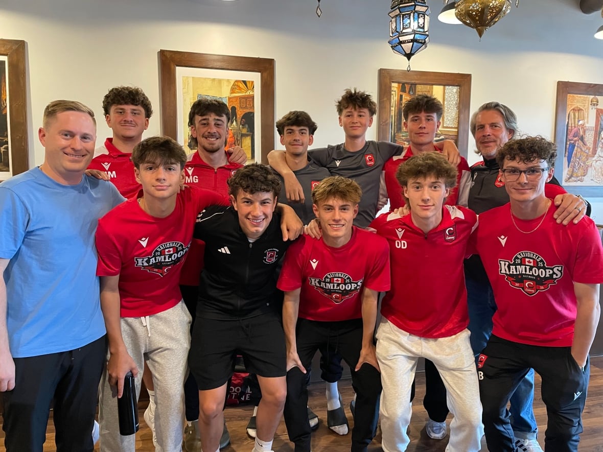 A group of 10 teenage boys in two rows smile with their arms around each other. On one end of each row is an adult coach. Most of the boys are wearing soccer jerseys or t-shirts.