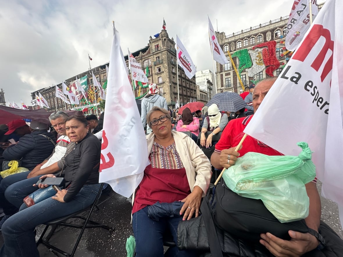A woman sits in a crowd of people holding a white flag belonging to the political party of Morena.