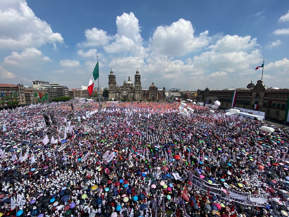 A view of the birds of a multitude of people, with white flags and balloons in the air, piled up on a central square.