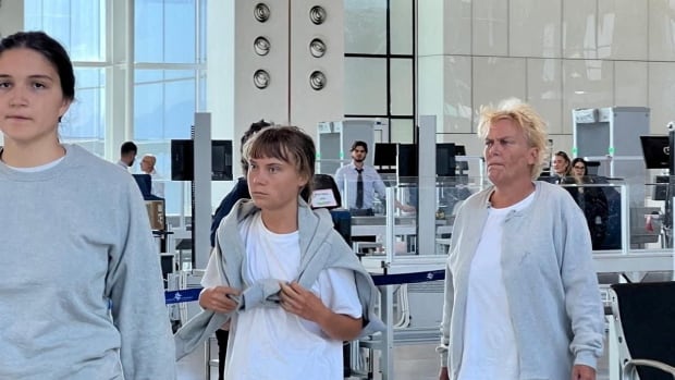 Three people wearing grey sweatpants are seen walking in an airport.