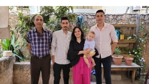 a woman holds a baby with three men around her on a balcony