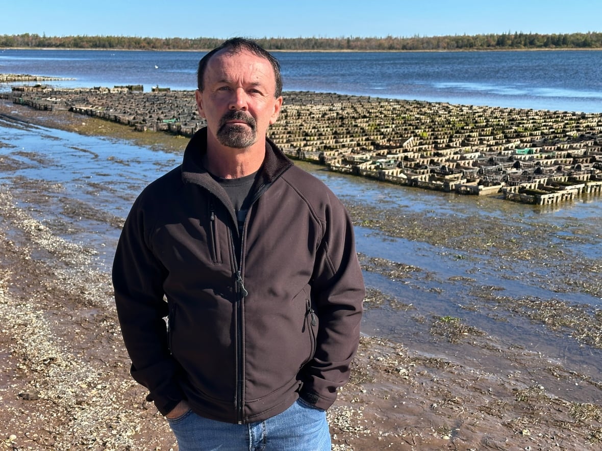 A man in a black jacket stands in front of rows of oyster traps.