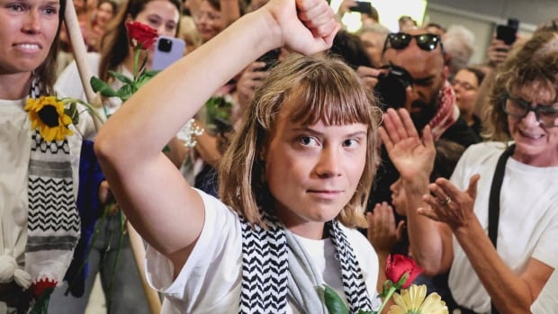 A young blond haired woman raises a fist as she is surrounded by many other people