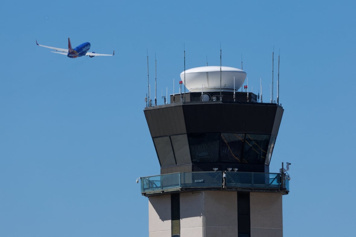 A plane in the sky that takes off next to a large air traffic control building