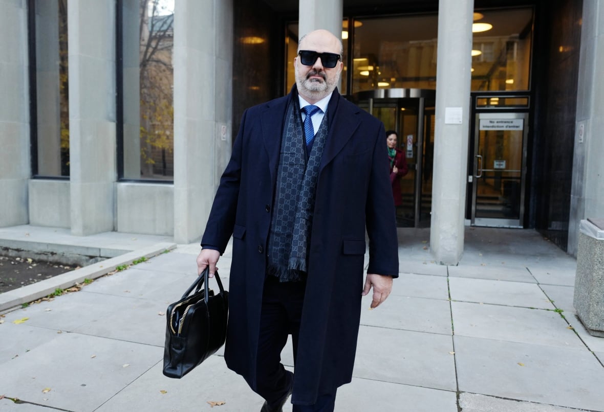 Un hombre con gafas de sol, traje oscuro y abrigo caminando fuera de un juzgado.