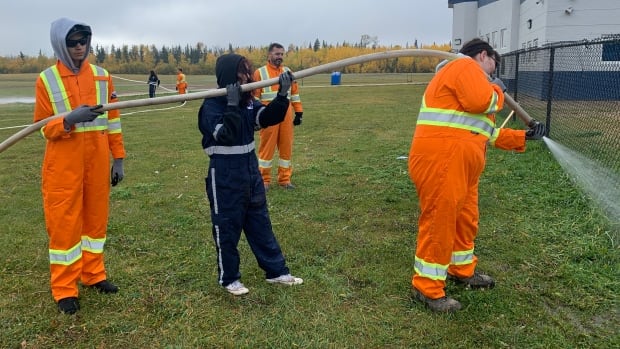 Three youth hold a fire hose and spray it into the ground for practice.