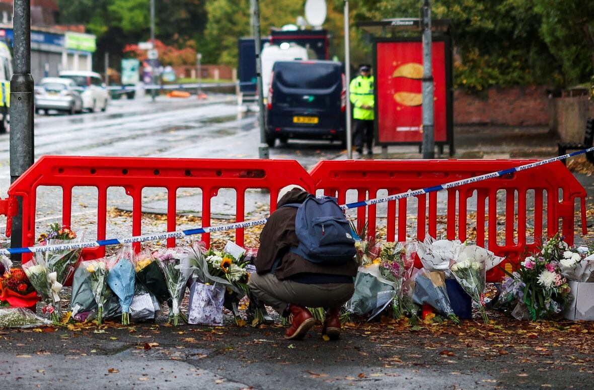 A person sitting next to the flowers that were left near the Manchester Church, where several people were killed on the day of forgiveness, while the police announced that it was a terrorist incident, in northern Manchester, Britain, October 4, 2025.