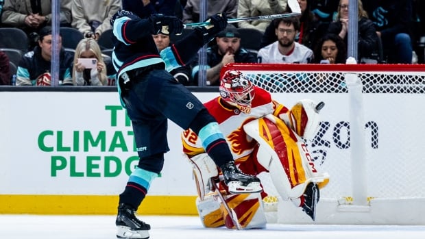 a close up of a hockey player shooting at the net, the goalie stopping the puck