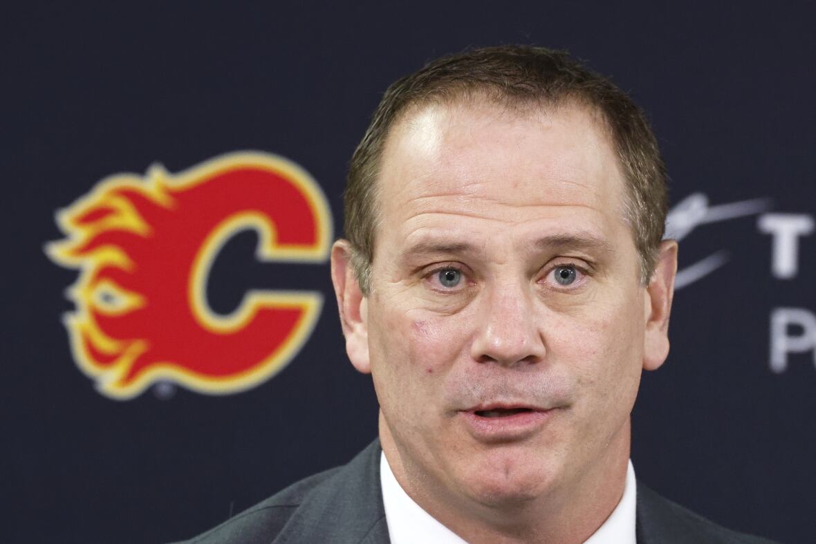 a close up of a middle aged white man with a flaming red C sign to his camera left