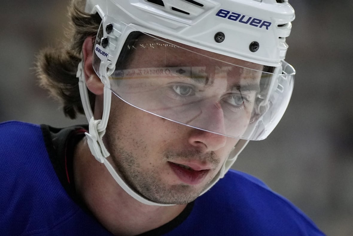 A close-up photograph of a hockey player wearing a white helmet with a clear visor.