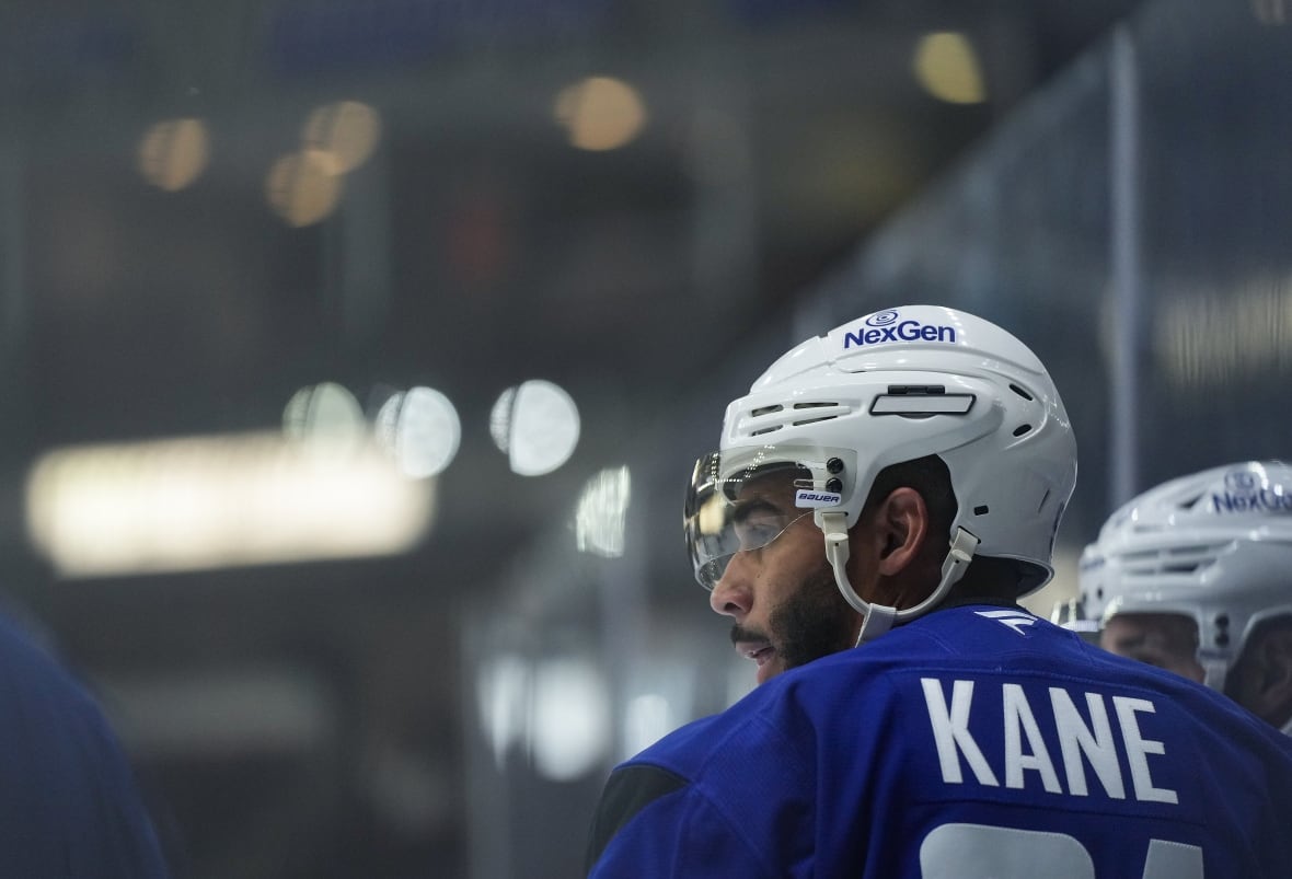 A hockey player wearing a blue jersey with the name 'Kane' on the back wears a white helmet with a clear visor.