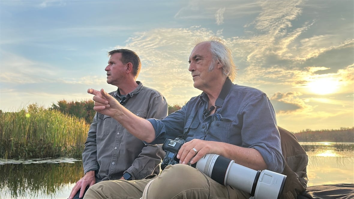 Two men on a boat at sunset, one holding a camera with large lens