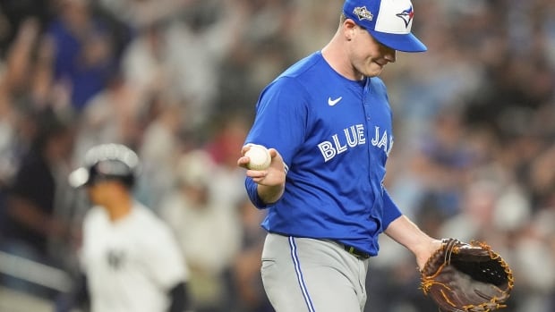 Player in blue shirt with blue jays written across chest holding a baseball and glove