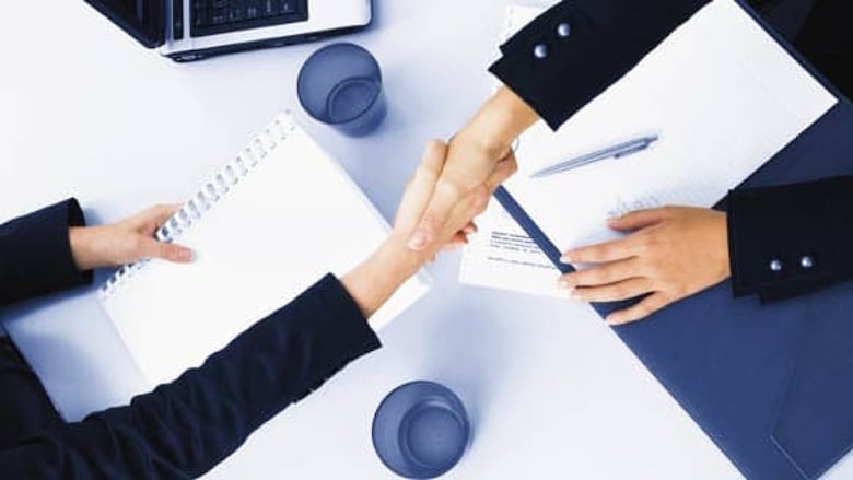 Two suited arms commence a handshake over a desk.