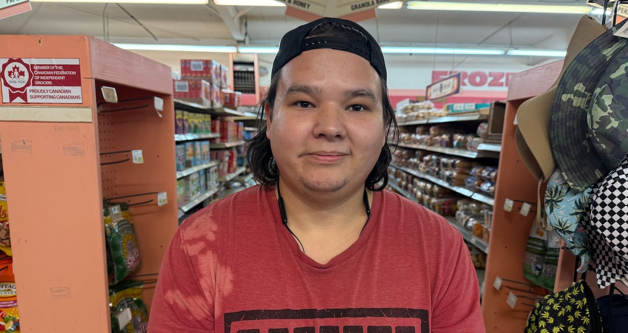 A young man in a red shirt stands in front of the shelves in a grocery store.