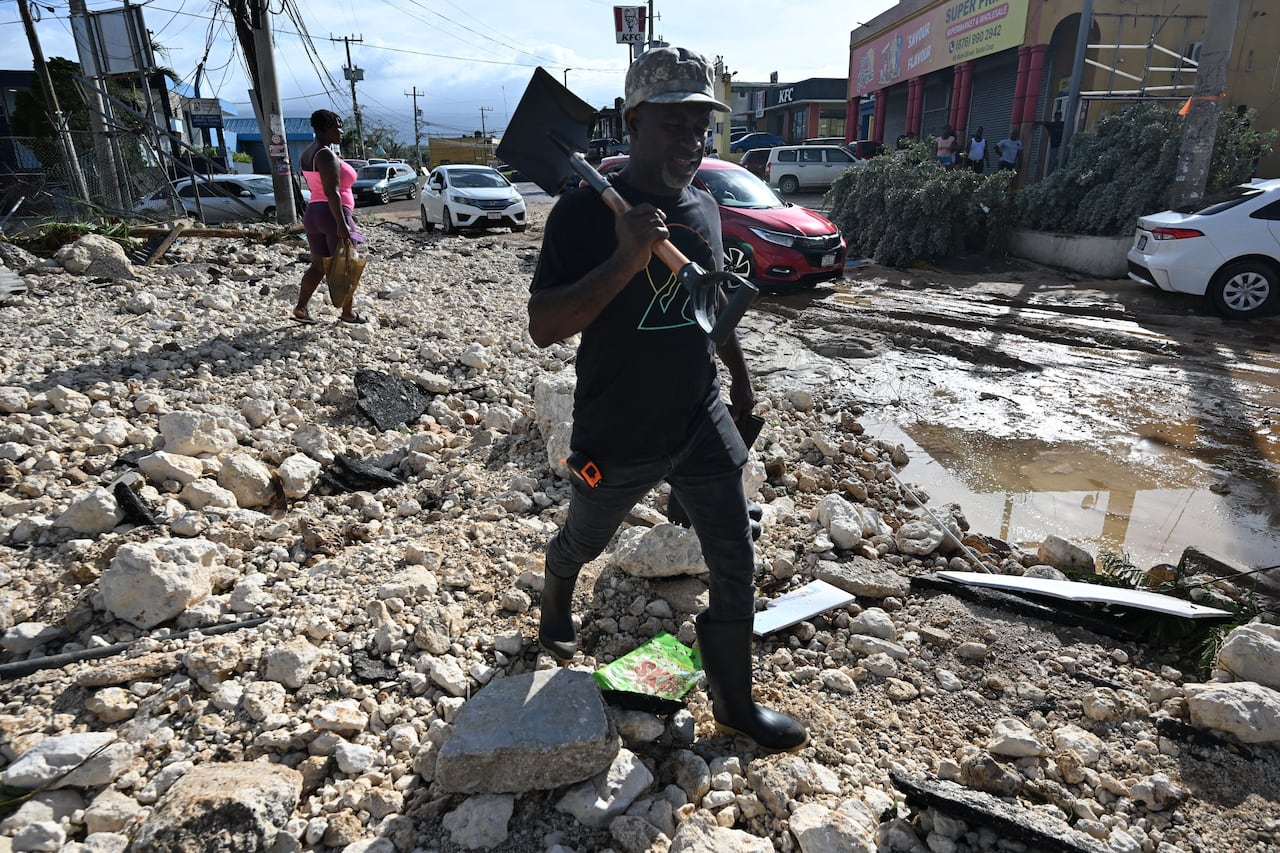 A man walks through debris with a shovel in hand on Main Street in Santa Cruz, St. Elizabeth, Jamaica on October 29, 2025. 